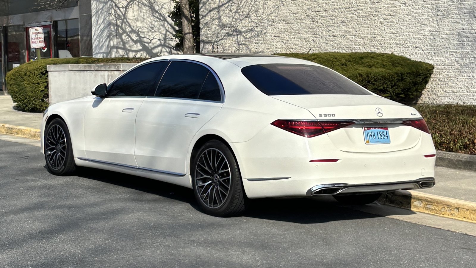 Sedán Mercedes-Benz S 500 Clase S blanco (generación W223) estacionado junto a una acera, visto desde atrás a la izquierda