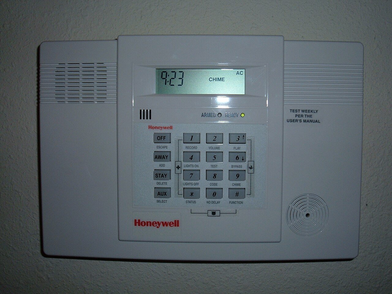 Panel de control de alarma de casa, blanco, montado en una pared, con pantalla que dice CHIME, teclado numérico y botones OFF, AWAY y STAY.