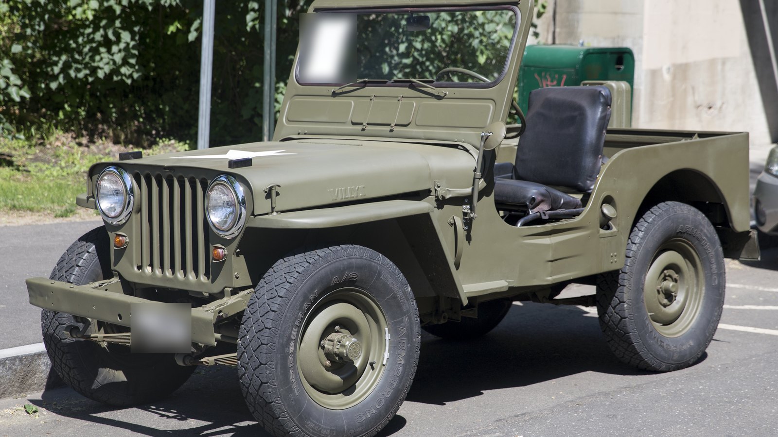 Willys CJ-2A de 1946 color verde olivo, vista delantera de tres cuartos desde la izquierda: parrilla de siete ranuras con los faros redondos dentro, guardafangos planos, parabrisas abatible, la palabra WILLYS estampada en el costado del cofre y caja trasera abierta, estacionado en una calle.