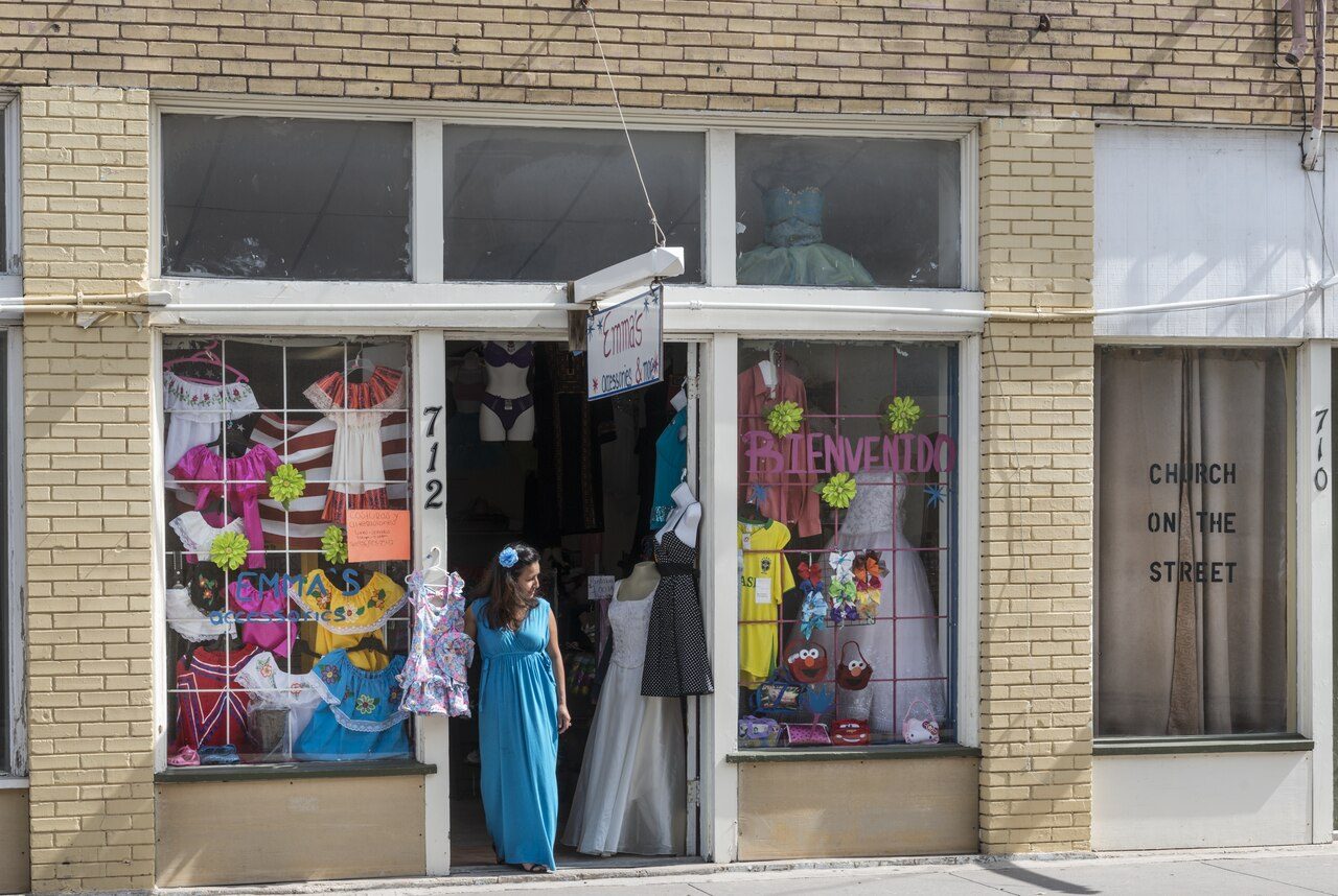 Una tienda de vestidos en el centro de Brownsville, Texas, con un letrero de Bienvenidos y vestidos de colores en la vitrina.